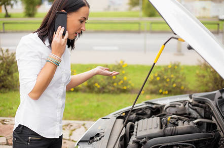 Woman chats on phone next to open hood after car breaks down. Photo by SHutterstock
