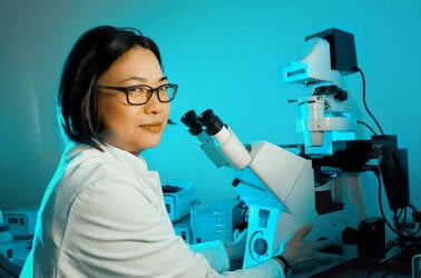 WHite lab coated scientist looks sceptical in front of microscope. Photo by Shutterstock