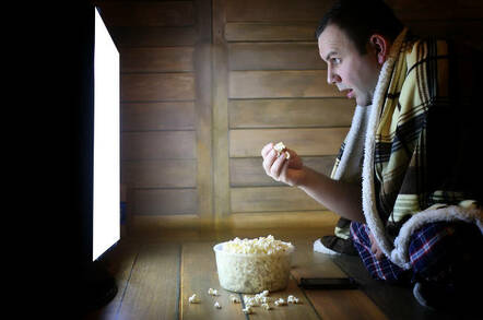 A man watching a screen and eating popcorn