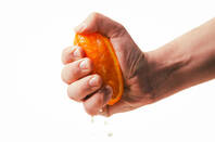 A hand squeezing juice from an orange