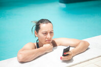 Annoyed-looking woman squints at mobile phone screen while in swimming pool.