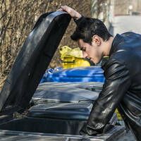 man in leather jacket rummages through bin 