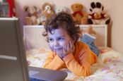 Child surrounded by stuffed animals watches video on computer 