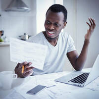 upset man looks at paper in front of laptop