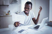 upset man looks at paper in front of laptop