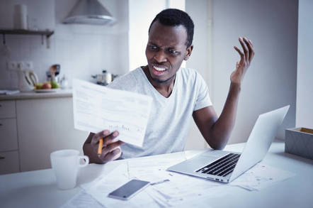 upset man looks at paper in front of laptop