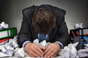Man bows head amongst piles of crumpled paper