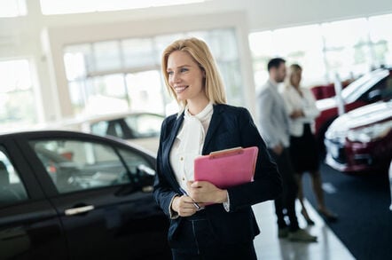 Car sales person walks away, smiling brightly, from couple looking at car...