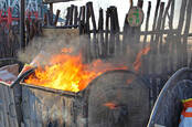 Dumpster fire against background of wooden fence with sad green recycling badged nailed to it