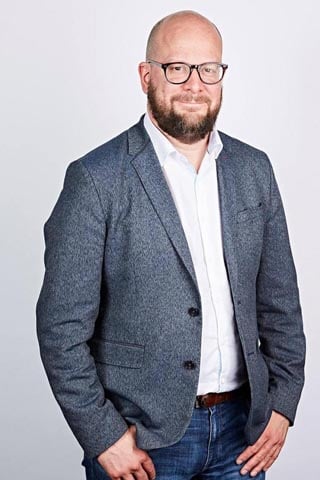 London's new chief digital officer, Theo Blackwell. Smiling bearded man in a tailored but loose mixed material jacket over jeans and a brown belt. 