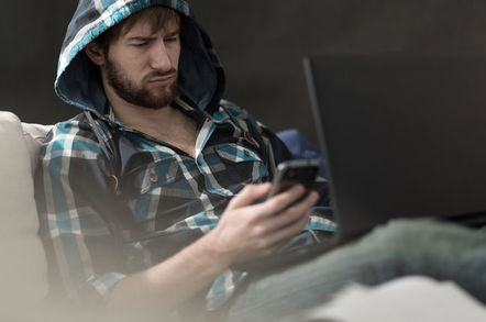 Bearded man in plaid hoodie looking annoyed holding smartphone