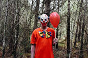 Creepy clown holding balloon in woods
