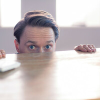 Scared looking office consultant hides under desk