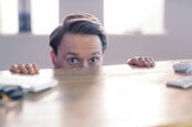 Scared looking office consultant hides under desk