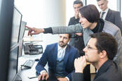 team of office workers peers at multiple monitors 