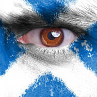 Angry man's eye peers from face painted with Scottish flag / st andrews cross