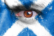 Angry man's eye peers from face painted with Scottish flag / st andrews cross