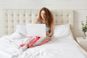 Woman sits in bed and works on laptop in her home.
