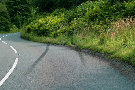 car crash skid marks on a rural road heading into the undergrowth