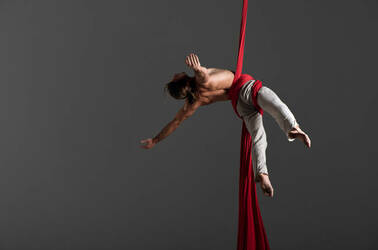 acrobatic yoga performed by man sliding down fabric