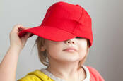 Studio portrait of funny baby girl in red baseball cap over gray wall background