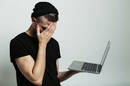 Young guy facepalms while holding a laptop