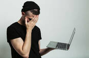 Young guy facepalms while holding a laptop