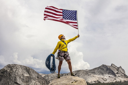 Climber waves an American Flag from the summit after a challenging ascent