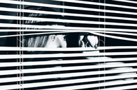 young woman looks through blinds