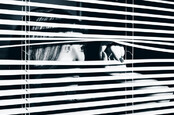 young woman looks through blinds