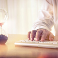 Man typing on computer keyboard next to hourglass