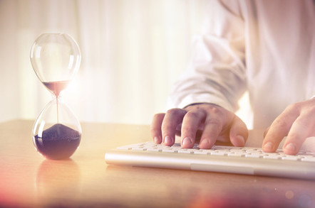 Man typing on computer keyboard next to hourglass