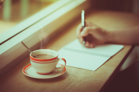 A coffee cup and hand writing in notebook