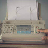An old fax machine with someone pushing a button