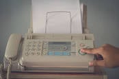 An old fax machine with someone pushing a button