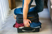 person sitting on suitcase to force it closed