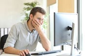 Man holds hand over mouth as he looks at monitor in a worried manner