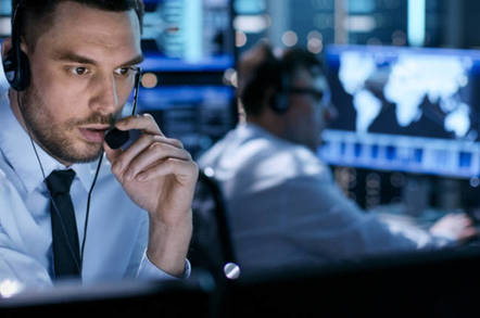 man in headset in fake fatigues sits in front of monitor, speaks intently to unseen officer