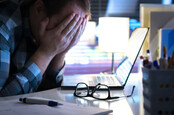 man in front of laptop puts head in hands - despairing