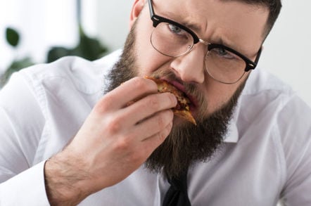 man in tie eats slice of pizza, looks sad while doing so
