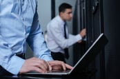 Man furtively types on laptop in server room
