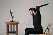 Angry man wields keyboard at a computer