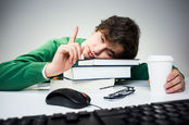 staffer props head on pile of books as he clicks a mouse and fights sleep