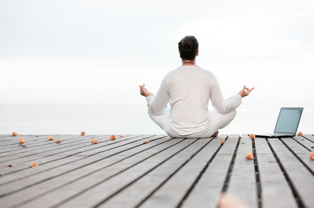 man meditating next to a laptop