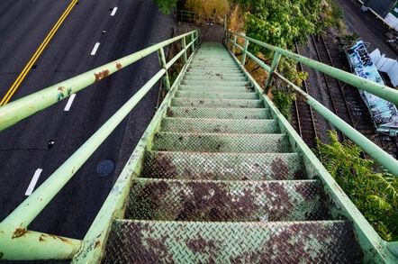 rusted stairs descend onto footpath between highway and train track