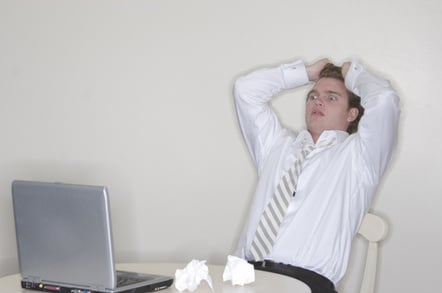 Young man in shirt and tie leans back, looks terrified, while looking at a monitor