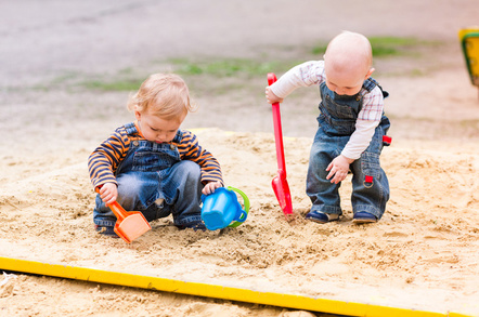 Two baby boys playing with sand in a sandbox