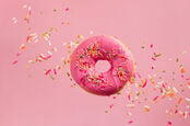 Iced pink doughnut flies through the air as it is showered with sprinkles