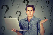 A man shrugs at a laptop with a background of question marks