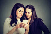 two women look disgusted at what they see on a phone screen